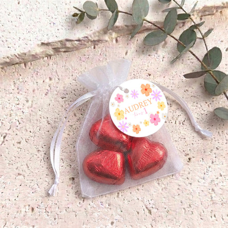 Pink organza pouch with drawstring, filled with red heart chocolates and a personalised round label.