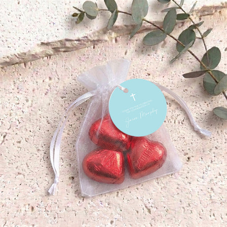 Translucent organza pouch with drawstring and red heart-shaped chocolates, with cross tag.