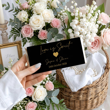 Favour Perfect personalised black and gold wedding chocolate bar with Love Is Sweet text held in a hand.