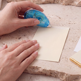 Double-sided tape applied to paper; blue tape dispenser held by hand